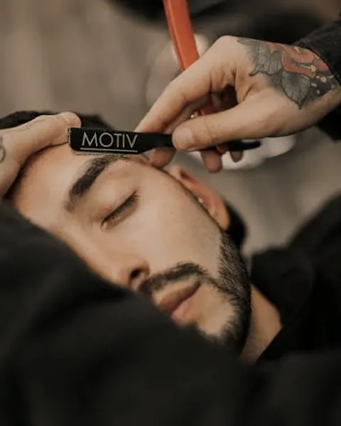 Barbero perfilando la ceja de un cliente con navaja.