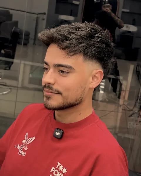Cliente con corte texturizado y barba corta, sentado frente al espejo.